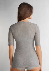 Haut gris à manches courtes en côte avec un col rond, présentant un design ajusté et un ourlet arrière légèrement plus long. La texture semble douce et extensible.