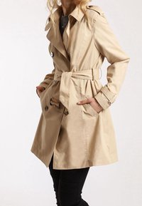 Beige trench coat med bälte i midjan, stora knappar och klassisk krage. Har två sidofickor och en knälång längd. Slät textur.