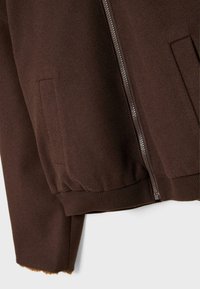 Giacca in fleece marrone con zip a lunghezza intera, polsini e orlo elastici, e tasche laterali. Tessuto morbido con un interno leggermente peloso.