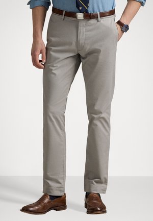 Mann trägt hellgraue Hose mit braunem Leder Gürtel, braune Leder Slipper, blaues hochgekrempeltes Hemd, gemusterten Krawatte und Armbanduhr.