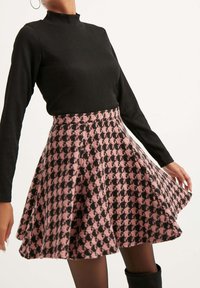 Schwarzes geripptes Langarmoberteil kombiniert mit einem fliederfarbenen und schwarzen Hahnentrittmuster-Rock aus strukturiertem Stoff.