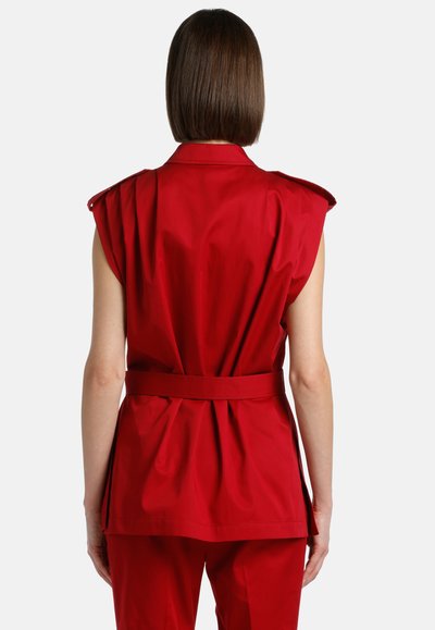 Red sleeveless jacket with shoulder tabs, belted waist, and gathered back detail. Made of smooth fabric with a structured fit.