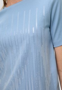 Light blue t-shirt with short sleeves, featuring a vertical pattern of silver sequins, soft cotton material, and a round neckline.