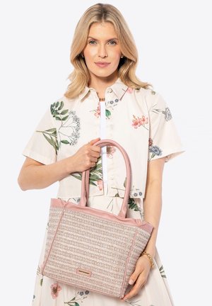 Mujer rubia con camisa de manga corta floral y falda, sosteniendo un gran bolso tejido rosa con asas dobles.