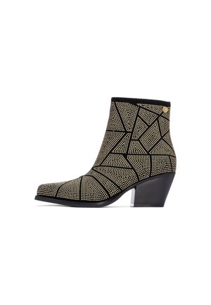 Botín negro hasta el tobillo con puntera afilada, que presenta un patrón geométrico de tachuelas doradas y un tacón cuadrado mediano, destacando una superficie texturizada.
