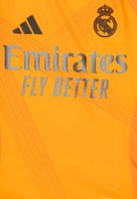 Maillot de sport orange avec le texte en relief gris « Emirates FLY BETTER » et le logo Adidas noir. Présente un tissu texturé et des accents de rayures diagonales.