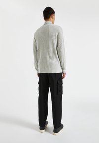 Suéter gris con canalé y cuello tipo alto, combinado con pantalones cargo negros con bolsillos laterales y zapatillas negras con suela blanca.