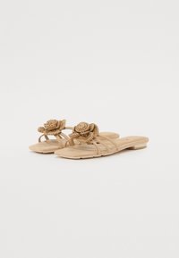 Beige flat sandals with multiple slender straps and a decorative woven flower at the front. Smooth texture and a minimalistic design.