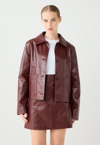 Bordeaux nep leren jack met een puntige kraag, twee voorzakken en knoopsluiting, gecombineerd met een bijpassende rok. Soepele textuur.