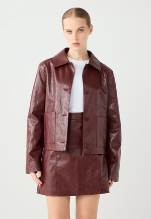 Giacca in faux leather borgogna con colletto a punta, due tasche frontali e chiusura a bottoni, abbinata a una gonna coordinata. Tessuto liscio.