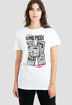 Frau trägt weißes T-Shirt mit schwarzen und weißen „One Piece“ Piraten-Gesucht-Plakaten und rotem Text auf der Vorderseite, steht vor einfachem Hintergrund.