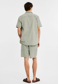 Randig grön skjorta och shorts set, korta ärmar, knäppningkrage, lös passform, tygtextur synlig, parat med bruna sandaler.