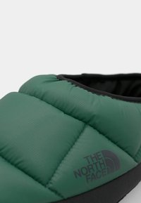 Green, puffy slipper with a textured quilted design. Features a black rubber sole and "The North Face" logo in dark gray.