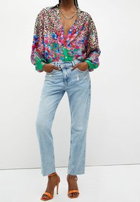 Monivärinen kukka- ja eläinkuvioinen paita, jossa napillinen edusta, yhdistetty vaalean pestyihin suoralahkeisiin farkkuihin, joissa koristeelliset taskuaccentit ja oranssit korkokengät.