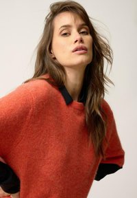 Suéter de punto rojo con mangas cortas y cuello negro. La textura parece suave, con un acabado sutilmente jaspeado.