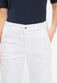 Pantaloni a strisce verticali bianchi con design aderente, dotati di chiusura frontale con bottone e tasche laterali. Realizzati in tessuto morbido, adatti per un abbigliamento casual.