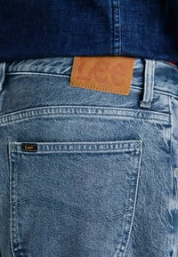 Hele helesinine denim püksid, millel on nahkpaneel, millel on "Lee" logo, tikitud tasku detailid ja tekstureeritud finishing.