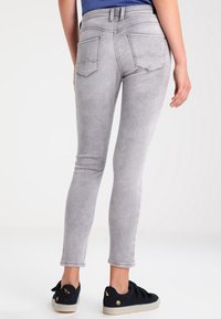 Jeans skinny grises con una cintura de altura media, ajuste slim, costuras sutiles en los bolsillos traseros y material de mezcla de algodón. Combinados con zapatillas negras.