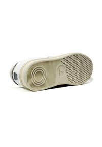 Suola di sneaker bianca con superficie in gomma testurizzata caratterizzata da motivi circolari e scanalati, punta arrotondata e dettaglio del logo vicino al tallone.