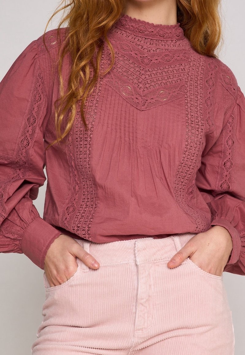 Rynkad blus med hög krage i dämpad ros med spetsdetaljer och veck; matchad med ljusrosa kordbyxor. Texturerad, mjuk bomullstyg.