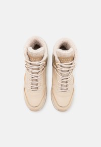 Baskets montantes beiges avec doublure en fausse fourrure, tige en cuir lisse, œillets en métal et lacets blancs contrastants. Logo de la marque sur la languette.