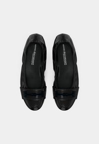 Ballerines noires en cuir avec côtés élastiques et une petite pièce métallique décorative à l'avant, avec des semelles intérieures de marque, montrées de dessus sur fond blanc.