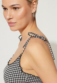 Zwart-wit gingham top met golvende randen, dunne verstelbare banden die in strikken zijn geknoopt, en een getailleerd ontwerp geschikt voor casual dragen.