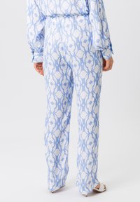 Lichtblauwe gemusterde broek van gladde stof. Beschikt over een groot abstract patroon in het wit en gedetailleerde accenten met een relaxte pasvorm.