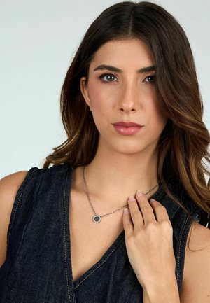 Collana d'argento con pendente circolare. Il modello indossa un top in denim scuro, con dettagli di catena visibili e un centrale pendente testurizzato.