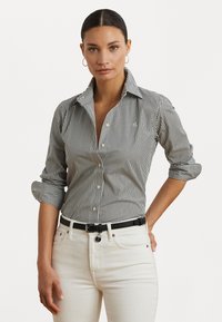 Musta-valkoinen raidoitettu nappipaita, jossa on kaulus, käännetyt hihat ja muotoiltu fit, yhdistettynä korkeavyötäröisiin valkoisiin farkkuihin ja mustaan vyöhön.