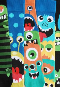 Trois paires de chaussettes présentant divers motifs de monstres colorés, avec des motifs comprenant des rayures, des pois, et plusieurs motifs d'yeux.