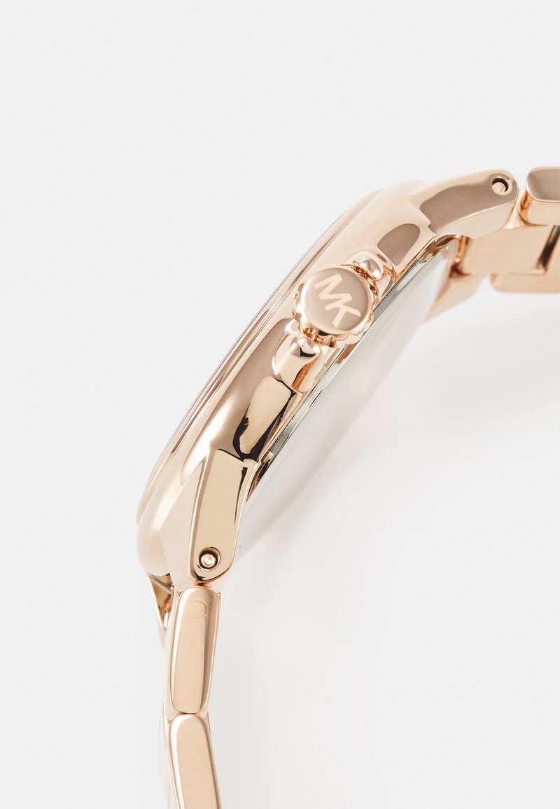 Guldtonad metallklocka med rund boett, enkel urtavla och länkarmband. Har en tryckkrone med en graverad logotyp och en polerad yta.