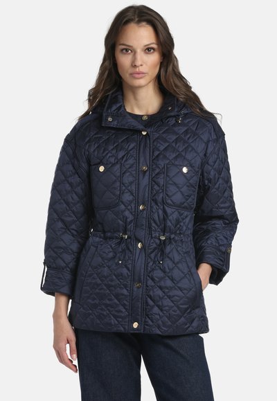 Marineblaue gesteppte Jacke mit Kordelzug in der Taille, zwei Fronttaschen und Druckknöpfen. Verfügt über einen hohen Kragen und endet oberhalb der Hüfte.