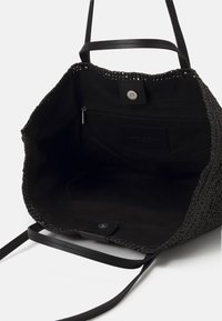 Zwarte gevlochten tas met leren handvatten, met een ruime binnenkant, een ritsvak en een drukknoopsluiting. Textuur en duurzame ontwerp.