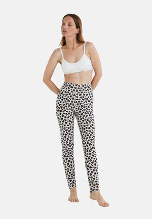 Leggings à imprimé léopard en blanc, dotés d'une taille haute, d'une coupe ajustée et d'une texture de tissu lisse. Associés à un soutien-gorge blanc décolleté.