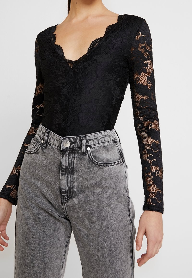 Body in pizzo nero con maniche lunghe, scollatura a V profonda, motivo floreale; abbinato a jeans in denim grigio chiaro a vita alta.