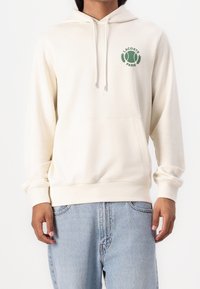 Krémová mikina s kapucí, klokaní kapsou, šňůrkou na kapuci a zeleným logem na hrudi. Měkká tkanina s žebrovanými manžetami a lemem.