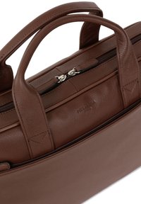 Bruine leren tote bag met dubbele handvatten, voorzien van een ritssluiting en een subtiele textuur op het oppervlak. Geen extra vakken zichtbaar.