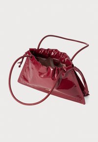 Red patent leather handbag with a gathered top, triangular shape, and thin shoulder strap. Features a smooth, glossy texture.