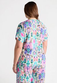 Camiseta de manga corta en multicolor con un vibrante patrón abstracto en rosa, morado, verde y azul sobre un fondo claro. Textura suave, corte relajado.
