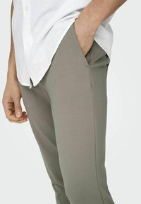 Pantalones gris claro hechos de una tela suave, con un corte ajustado y bolsillos laterales, combinados con una camisa blanca de botones.