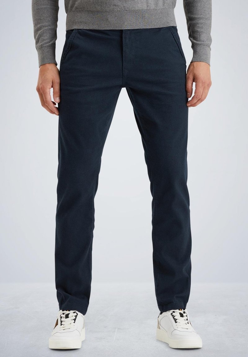 Pantalons en velours côtelé bleu marine avec une coupe fuselée, dotés de poches avant et d'une surface texturée, associés à des baskets blanches.