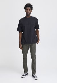 Camiseta negra de manga corta con un bolsillo en el pecho, combinada con pantalones verde olivo y zapatillas negras con detalles blancos.