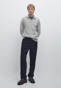 Grijze pullover met een kraag, gecombineerd met marineblauwe broek en bruine veterschoenen. Eenvoudige, gladde textuur en een ontspannen pasvorm.