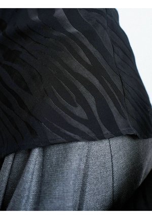 Primer plano de tela negra texturizada con un sutil patrón de cebra sobre tela gris tejida, resaltando los detalles textiles y las costuras.