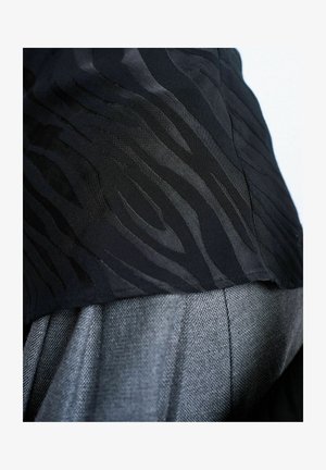 Gros plan sur un tissu noir texturé avec un motif zèbre subtil sur un tissu gris tissé, mettant en valeur les détails du textile et les coutures.
