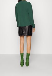 Grön tröja, svart läder minikjol och gröna mocka ankelstövlar med klackar. Outfitten har en enkel, figurnära design och kontrasterande texturer.