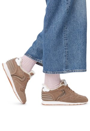 Person wearing light pink socks and beige fur-lined sneakers with white soles and blue denim wide-leg jeans.