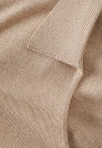 Beige Strickpulloverstoff mit feiner Textur und glatter Oberfläche, ausgestattet mit einem umgeschlagenen Kragen und sauberen Kanten. Dezente Farbvariationen.