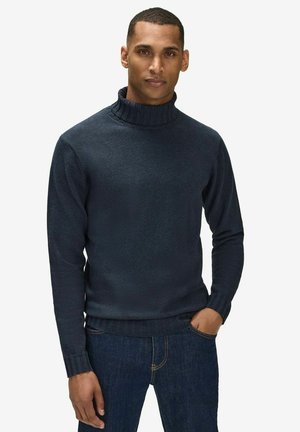 Mörkblå stickad polotröja med ribbat krage och muddar, med en slät textur och figurnära design. Bärs med mörkblå jeans.